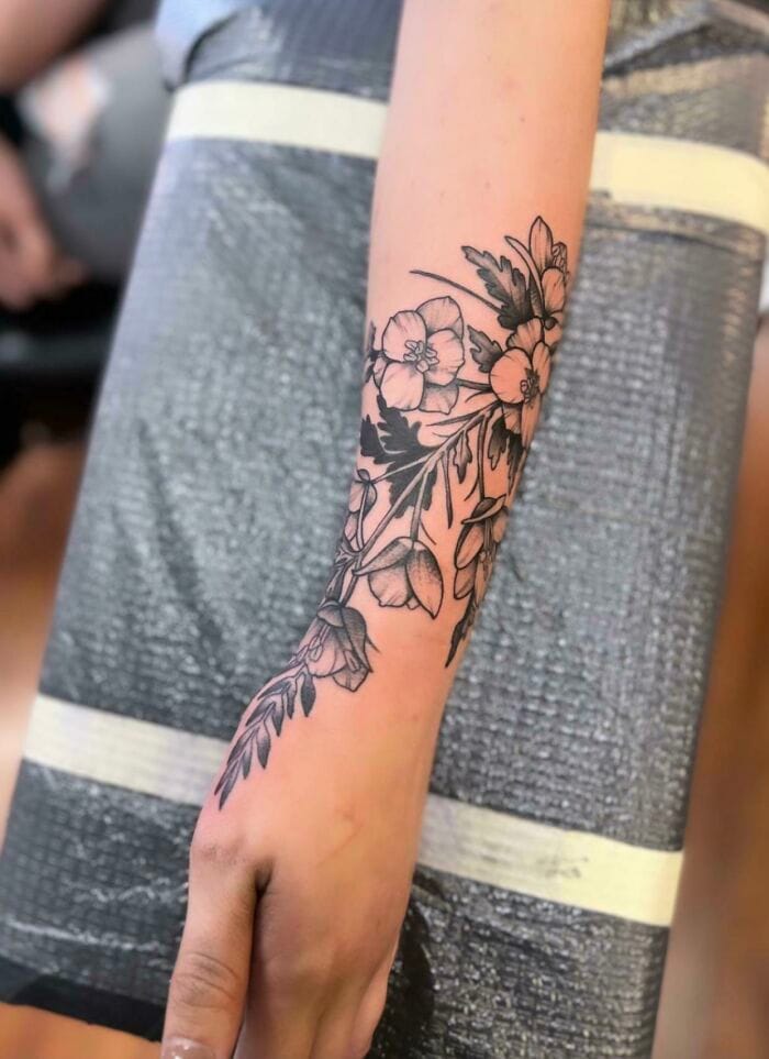 Delicate botanical artistry cascades down this forearm like nature's own calligraphy, featuring intricately detailed flowers and foliage rendered in fine black linework. The organic composition flows seamlessly from wrist to elbow, creating a stunning sleeve that celebrates the timeless beauty of floral motifs with contemporary tattoo craftsmanship. 🌸