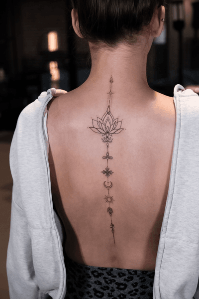 A delicate spine tattoo transforms into a meditation on spiritual ascension, featuring an intricate lotus bloom that cascades down the back through geometric symbols and sacred elements. The fine line work creates an almost ethereal quality against the skin, while each carefully placed symbol tells its own story of enlightenment and growth. ✨ This vertical masterpiece perfectly follows the natural curve of the spine, turning the body into a canvas for mindful artistry.