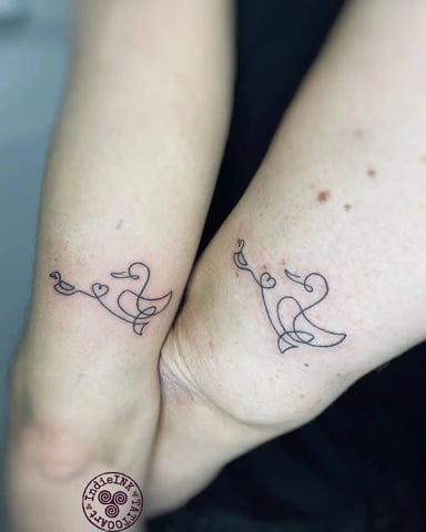 Two delicate line-drawn ducks create an adorable matching tattoo set, with each bird facing toward the other when the arms are brought together. The minimalist black ink design features sweet heart details that add a romantic touch to these playful waterfowl companions 🦆 Perfect for couples, friends, or siblings who want to celebrate their unbreakable bond with something both whimsical and meaningful.