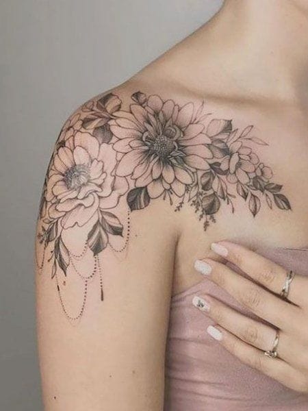 Delicate floral artistry cascades across the shoulder and collarbone in this stunning black and grey piece, featuring intricately detailed blooms that seem to bloom naturally from the skin. The artist's masterful use of dotwork and fine linework creates gorgeous texture in each petal, while dangling ornamental details add an elegant finishing touch that perfectly complements the feminine placement 🌸