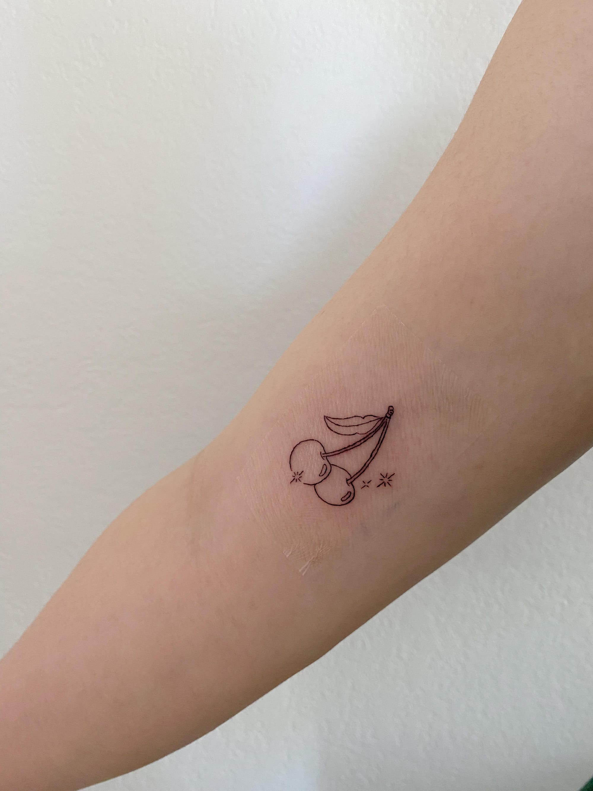 Delicate line work transforms two simple cherries into a whimsical piece of edible art on this forearm placement. The minimalist black ink design captures that perfect balance between sweet innocence and subtle sass, while tiny decorative stars add just the right amount of sparkle ✨ Fine line tattoos like this prove that sometimes the smallest details make the biggest statement.
