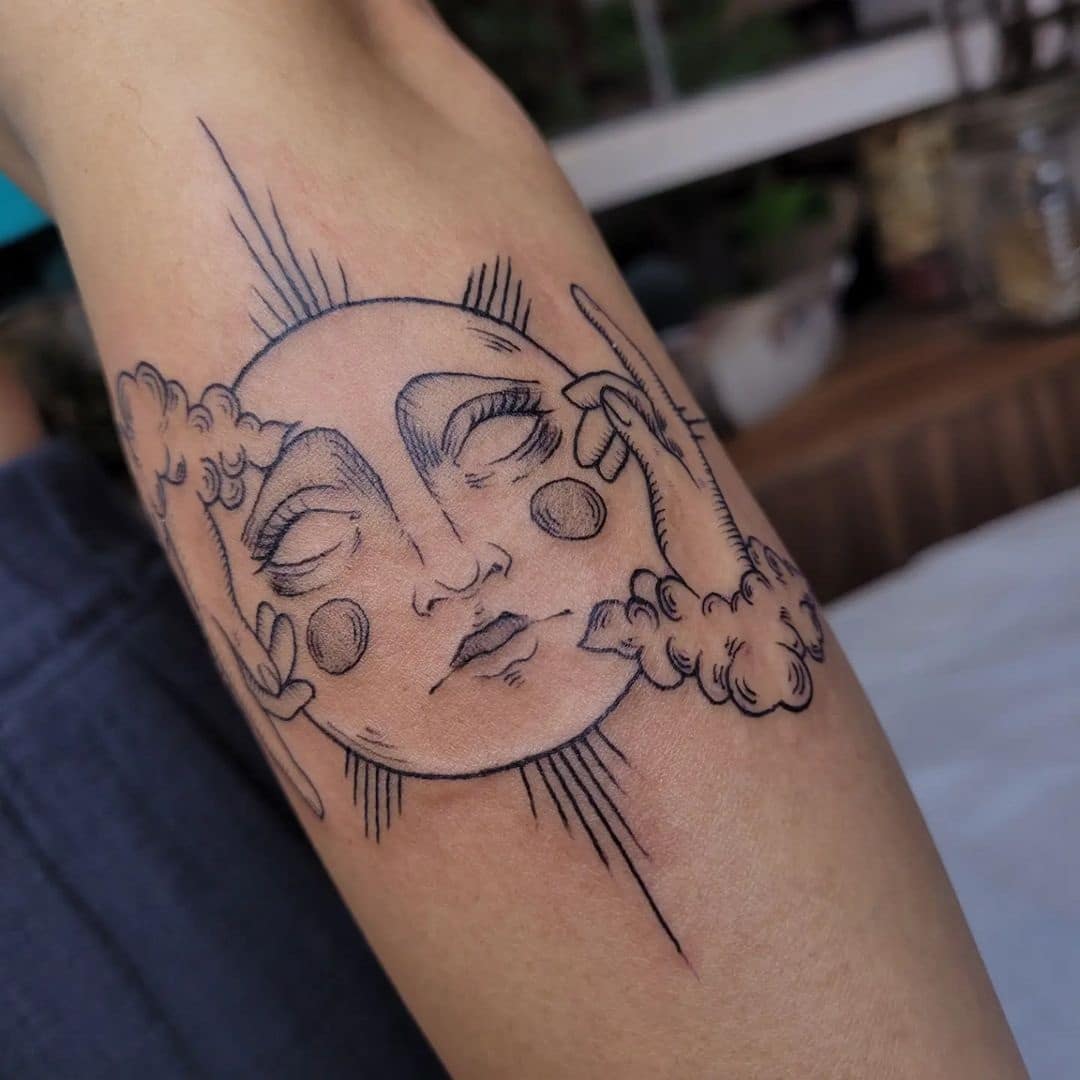 Celestial drama unfolds on skin with this captivating sun and moon fusion, where flowing clouds dance around a serene face adorned with delicate line work rays. The fine black ink creates beautiful contrast through varying line weights, transforming the forearm into a canvas for this dreamy astronomical portrait that feels both mystical and grounded ☁️