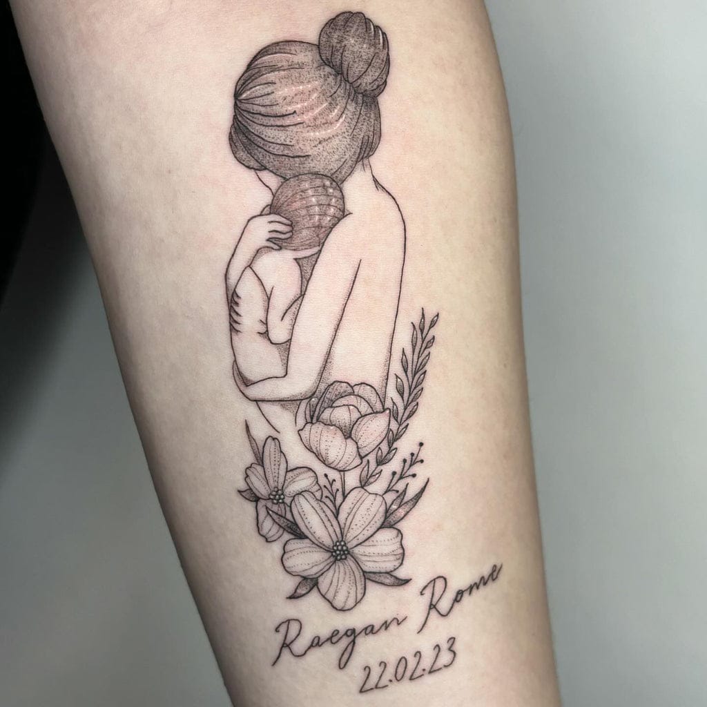 Delicate line work captures an intimate moment between mother and child in this touching memorial piece 💕 The soft botanical elements—roses and delicate florals—create a beautiful frame around the embracing figures, while the script lettering and date below add deeply personal significance. Positioned on the forearm, this fine-line tattoo transforms grief into art with its gentle, minimalist approach to honoring someone special.