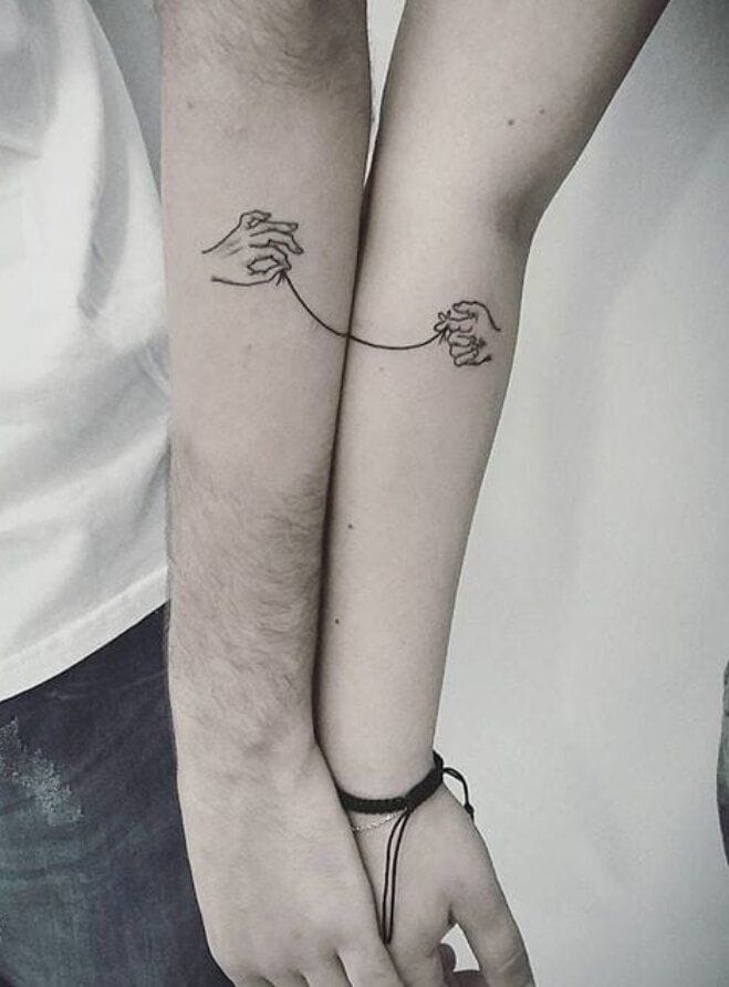 Connection transcends physical distance in this beautifully executed matching tattoo design 🤝 Two delicate hands reach across separate forearms, linked by a fine line that creates the illusion of an unbreakable bond when the arms are brought together. The minimalist linework and strategic placement transform individual tattoos into one cohesive piece of body art that celebrates partnership and unity.