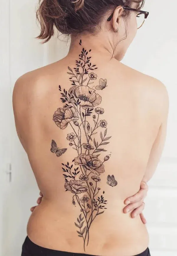 Delicate botanical artistry cascades down this woman's spine in stunning black linework, featuring intricate poppies, wildflowers, and dancing butterflies that seem to grow naturally from her lower back to shoulders. The fine-line technique creates an almost ethereal quality, while the central placement transforms her back into a living garden canvas. 🌸 Perfect inspiration for anyone dreaming of feminine floral spine art with serious botanical vibes.
