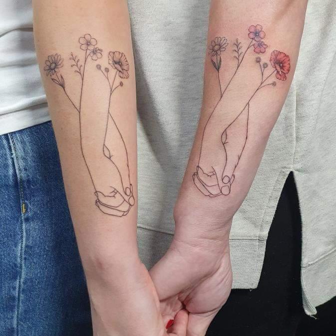 Delicate line work transforms two forearms into a botanical love story, where intertwined hands bloom into graceful wildflower stems 🌸 The minimalist design features soft poppies and cosmos in muted tones, creating a romantic matching set that celebrates both connection and growth. When held together, these complementary tattoos form a complete garden that literally grows from the couple's bond.