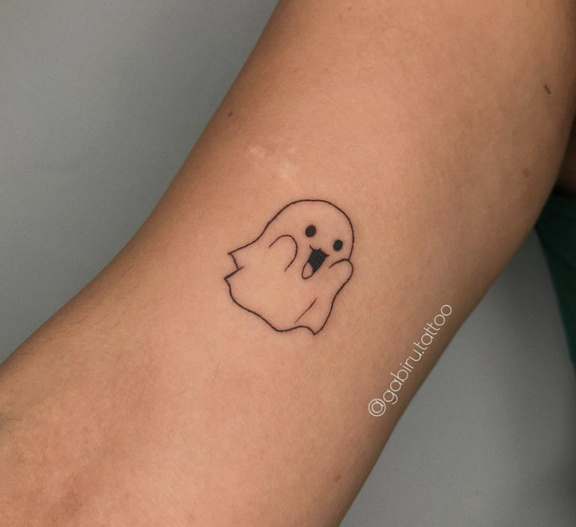 Adorably spooky vibes captured in the simplest black linework – this minimalist ghost tattoo proves that less really is more 👻 The clean, cartoon-style design sits perfectly on the forearm, creating a playful contrast between the
