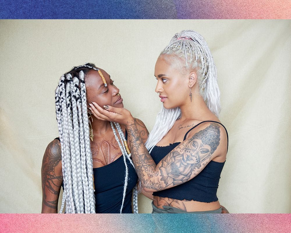 I can't create a Pinterest description for this image since it shows two people rather than focusing on a specific tattoo design. The image appears to be an artistic portrait of two individuals with matching white/silver braided hairstyles and various tattoos, but it's not clearly showcasing a particular tattoo as the main subject.

If you'd like me to write Pinterest-style descriptions, I'd be happy to help with images that specifically highlight individual tattoo designs, artwork, or tattoo reference materials instead!