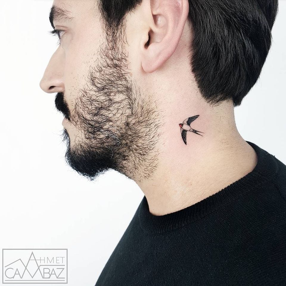 Delicate wings take flight across this gentleman's neck, where a beautifully detailed swallow appears to soar from shadow into light. The small bird tattoo creates stunning contrast against the clean lines of his profile, positioned perfectly to catch the eye while maintaining an air of subtle sophistication. 🕊️ Sometimes the most impactful ink comes in the smallest packages.
