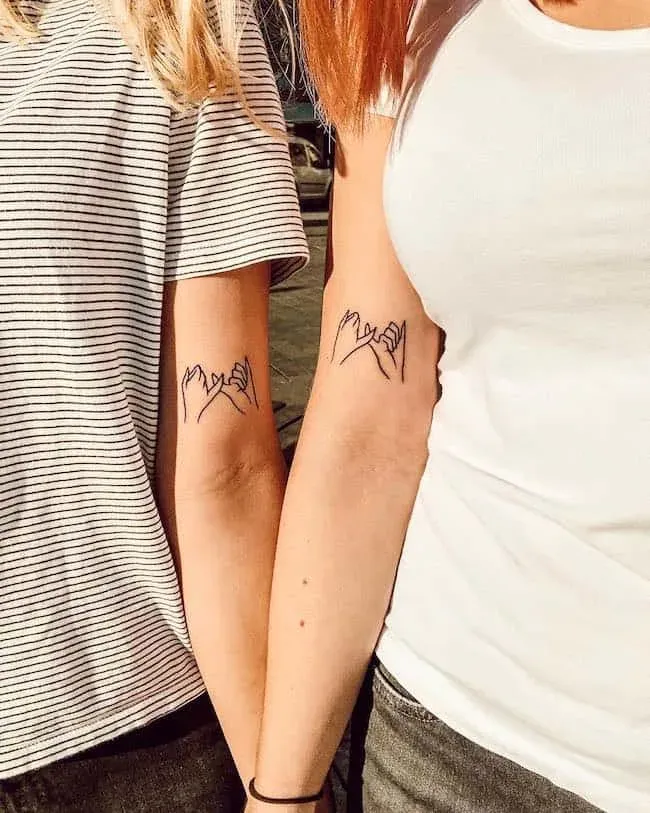 Friendship bonds made permanent through matching pinky promise tattoos that capture the sweetness of childhood vows in elegant black linework. The minimalist design features two hands with interlocked pinkies, symbolizing unbreakable trust and loyalty between these two friends. Positioned on the forearms where they're always visible, these tattoos serve as daily reminders of their special connection 🤝