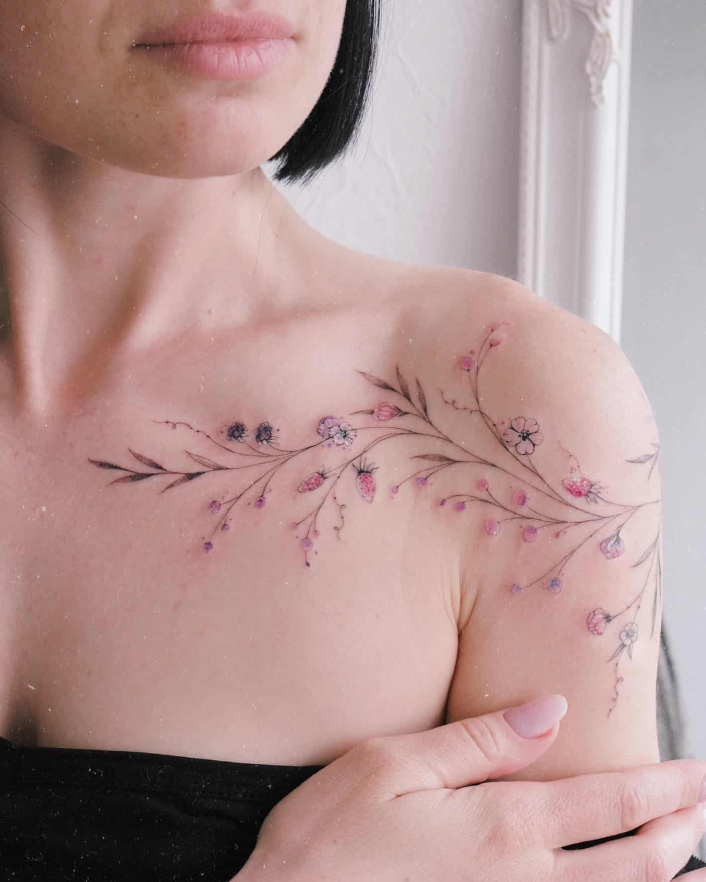 Delicate botanical artistry blooms across the shoulder and chest in this ethereal floral tattoo, where soft pink and purple wildflowers seem to grow organically along graceful vine-like stems. The watercolor-inspired technique creates an almost painted effect, as if nature itself has left its gentle mark on skin 🌸 Perfect placement allows the design to flow naturally with the body's curves, creating a feminine and dreamy aesthetic.