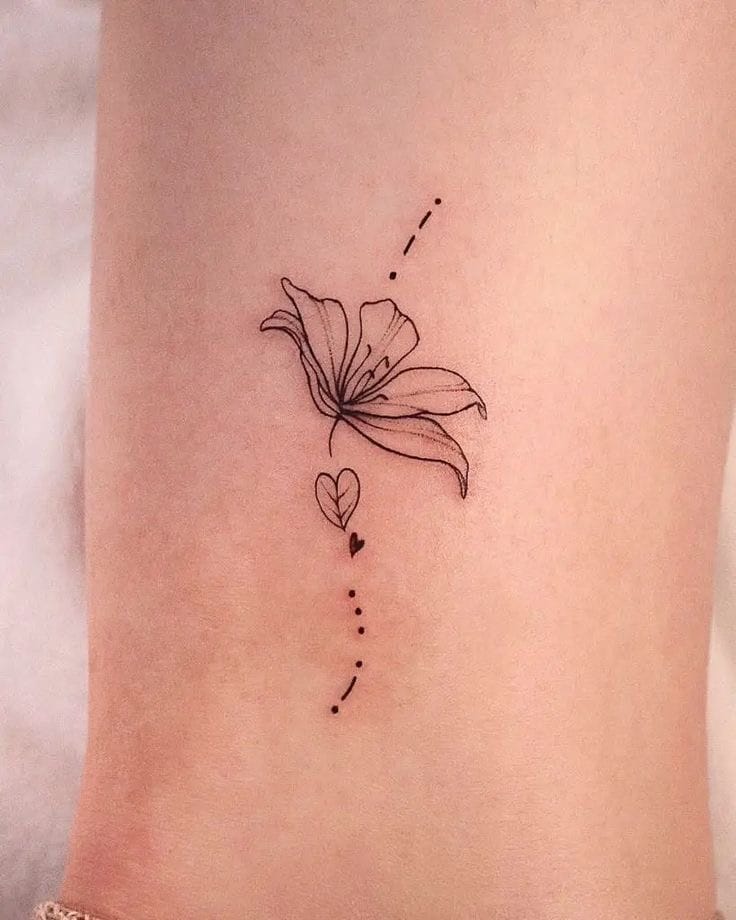 Delicate line work transforms skin into poetry with this minimalist lily tattoo, where a single bloom sits gracefully between dotted trails that dance up and down the torso. The tiny heart detail nestled within the design adds an intimate touch to what's already a stunning example of botanical fine-line artistry 🌸 Perfect placement that follows the body's natural curves while maintaining elegant simplicity.