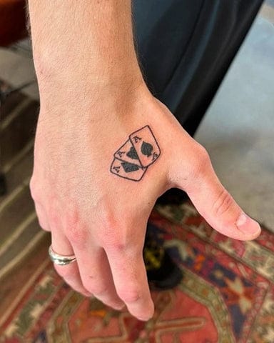 Bold lines frame a classic blackjack hand on this perfectly placed hand tattoo - because sometimes you've got to show your cards. The crisp, minimalist design captures the thrill of hitting 21 with an ace and face card combo that's both lucky and stylish. 🃏 Simple yet striking, it's the kind of ink that speaks to risk-takers and card sharks alike.