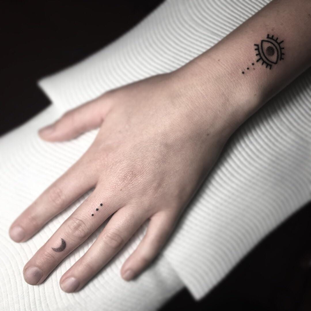 Delicate celestial minimalism takes center stage with this enchanting hand tattoo featuring an all-seeing eye on the wrist and a crescent moon adorning the ring finger. The scattered dots create a mystical constellation effect that flows beautifully across the skin, while the fine line work demonstrates exquisite restraint and artistry ✨ Perfect placement for those who want their spiritual symbols to be both visible and elegantly understated.