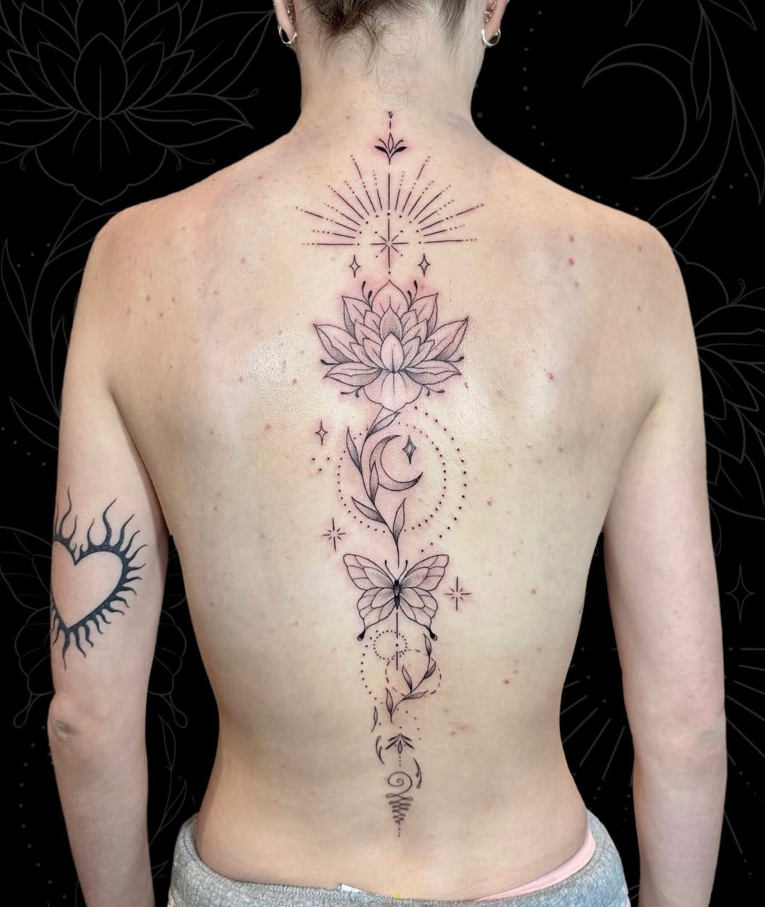 Cascading down the spine like a sacred river, this intricate linework masterpiece weaves together celestial sunbursts, blooming lotus petals, crescent moons, and delicate butterflies in perfect harmony. The fine-line technique creates an ethereal quality that seems to dance across the skin, while the vertical composition emphasizes the body's natural curves ✨ A stunning example of how botanical and celestial elements can unite to tell a story of transformation and spiritual growth.