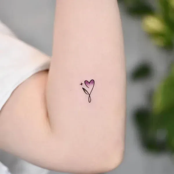 Delicate black linework transforms into pure poetry with this minimalist heart-topped stem design, perfectly positioned on the inner arm where it feels like a secret love letter to yourself. The subtle purple fill adds just enough color to make this tiny botanical beauty pop against the skin, proving that the most meaningful tattoos don't always need to shout to be heard 💜