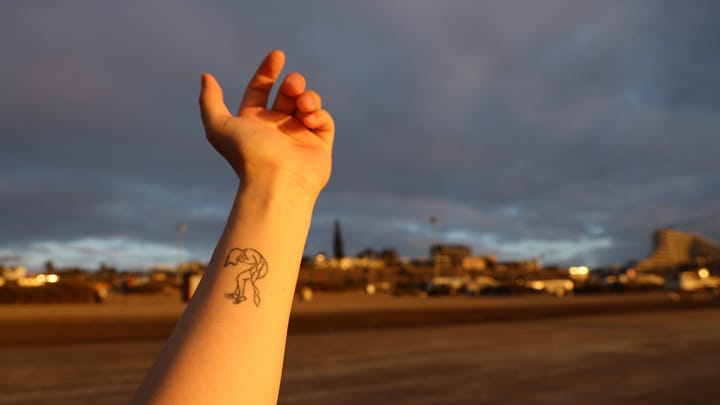 person with black tattoo on left hand